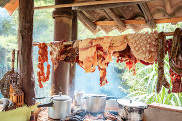 Smoked Meats Hanging Above Wood-Fired Stove in Rustic Outdoor Kitchen