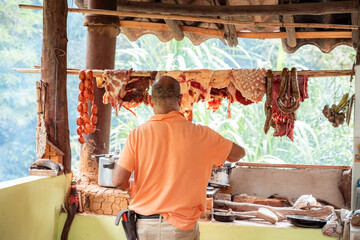 Man cooking in a rustic Colombian kitchen with hanging meats