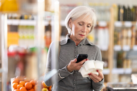 Checking expiration date of yogurt - elderly female shopper scans QR code on label of yogurt using her smartphone