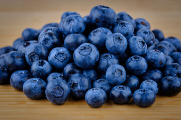Fresh ripe blueberries piled on wooden table, close-up macro shot of organic healthy berries with vibrant blue color and natural bloom, perfect for backgrounds, recipes, or healthy food concepts.