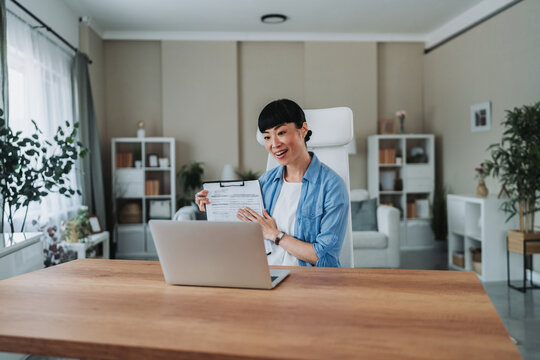 Asian freelancer woman showing contract during video call at home office