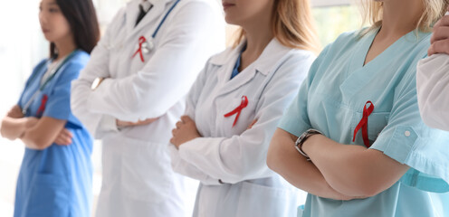 Professional team of doctors with red ribbons in clinic, closeup. World AIDS Day concept