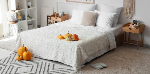 Interior of light bedroom with pumpkins and autumn leaves