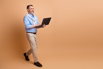 Confident businessman walking with a laptop on a beige background, showcasing professional style and confidence