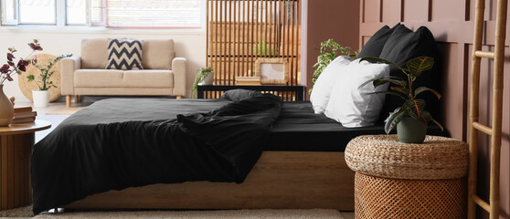 Interior of stylish bedroom with black linen, folding screen and sofa