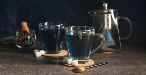 Teapot and cups of butterfly pea flower tea on grunge background