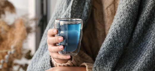 Woman with cup of tasty blue tea at home, closeup