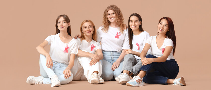 Beautiful women with pink ribbons sitting on beige background. Breast cancer awareness concept