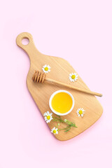Wooden board with bowl of honey and chamomile flowers on pink background