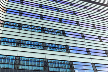 A modern building with a sleek design featuring repeating horizontal lines and reflecting blue sky in the multiple windows, from a low angle.