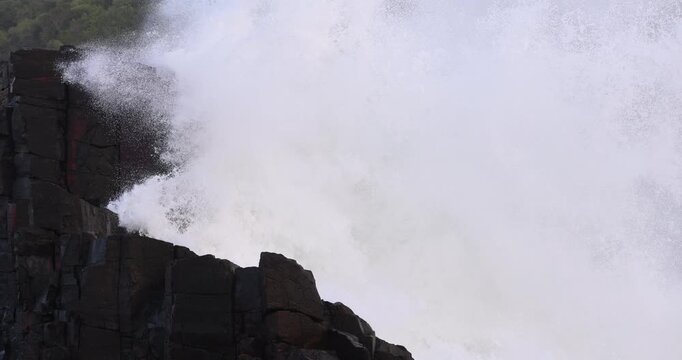 A huge white wave crashes and explodes into a large basalt rock formation. Captured in slow motion during an east coast low storm swell event.