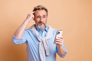 Confident senior businessman analyzing his smartphone while standing against a beige backdrop