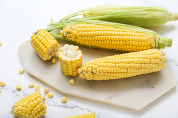 Board with fresh corn cobs on white marble table, closeup