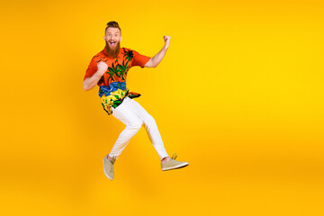 Obraz premium Excited young man in tropical shirt jumping joyfully against a vibrant yellow background with a delighted smile