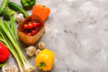 Paper bag with tomatoes, fresh vegetables and mushrooms on grunge grey background