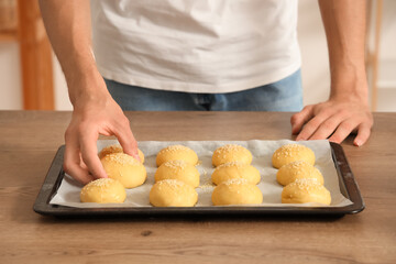 Handsome young man with tray of fresh raw buns in bakery
