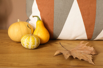 Pumpkins with fallen leaf and pillow on shelf in room, closeup