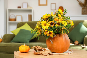 Pumpkins with flowers and fallen leaves on table in living room
