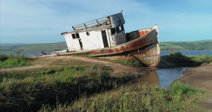 The Point Reyes shipwreck, a weathered fishing boat, rests on the sandy shore in Inverness, California, USA. Its aged wood and peeling paint tell a story of time.