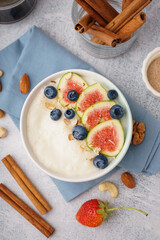 Bowl of tasty semolina porridge with berries and figs on white background