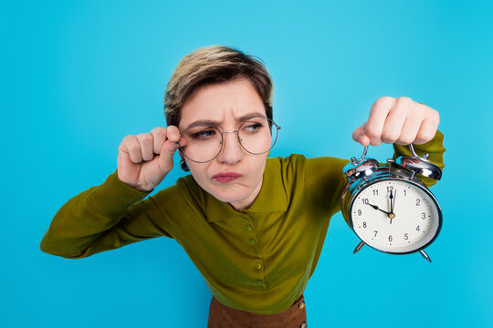 Young female professional holding an alarm clock with an expression of curiosity, wearing casual khaki shirt and glasses