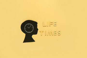 Text LIFE TIMES and cutout paper human head with clock on yellow background. Top view