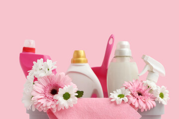 Basket with cleaning supplies, tools and spring flowers on pink background