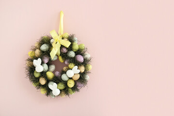 Beautiful Easter wreath decorated with eggs and feather on pink wall