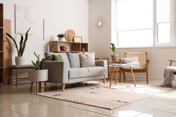 Interior of cozy living room with sofa, shelving unit and houseplants near white wall