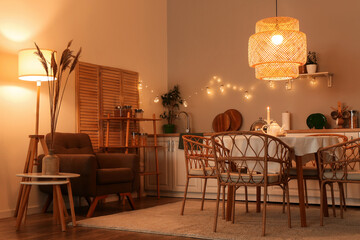 Interior of modern kitchen with glowing lamps, table, white counters and chairs at evening
