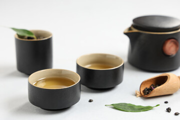 Teapot with cups, wooden scoop of dry tea and leaves on white background
