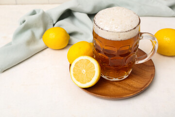 Glass of fresh beer and wooden plate with lemons on white table