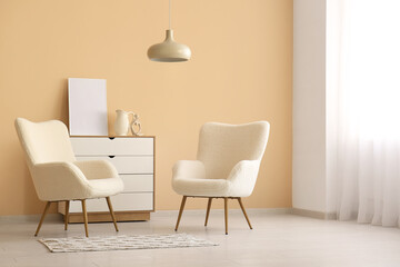 Cozy armchairs and chest of drawers near beige wall