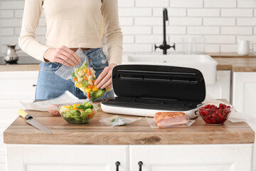 Young woman with vacuum sealer machine for food, meat and vegetables in packs on kitchen table