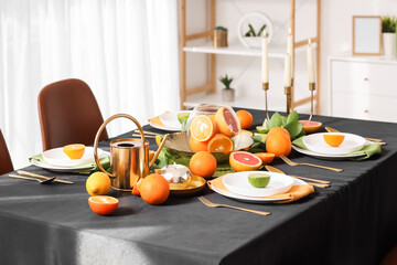 Beautiful table setting with citrus fruits, burning candles and black tablecloth in living room