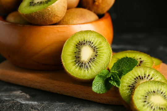 Wooden board and bowl with fresh kiwi on black background
