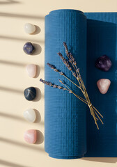 A rolled blue yoga mat with lavender sprigs and various crystals on a light beige surface