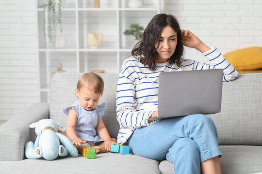 Cute baby and happy young mother working with laptop on maternity leave at home