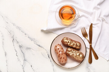 Plate with tasty eclairs, cutlery and cup of tea on light background