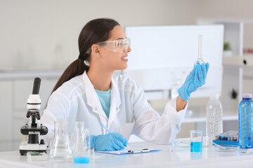 Fototapeta premium Female young scientist with professional glassware of water samples writing on clipboard in research laboratory