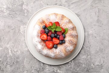Tasty Bundt cake with powdered sugar and berries on grey textured table, top view