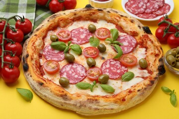 Delicious pizza with salami, olives, tomatoes and basil on yellow table, closeup