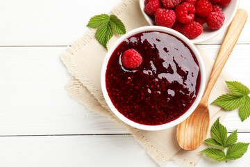 Sweet raspberry jam in bowl and berries on white wooden table, flat lay. Space for text