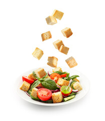 Croutons falling into bowl of salad against white background