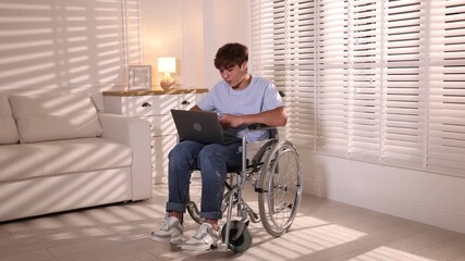 Smiling teenage boy in wheelchair having videochat by laptop at home - Powered by Adobe