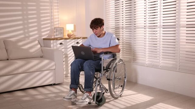 Smiling teenage boy in wheelchair having videochat by laptop at home