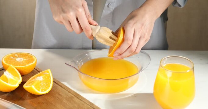 Making juice. Woman with orange using wooden juicer at white marble table, closeup