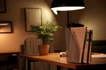Holder with newspapers on desk in dark office, closeup