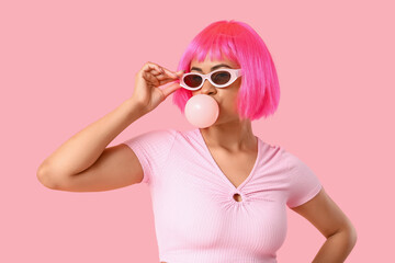 Beautiful young African-American woman in stylish pink wig blowing bubble gum on color background