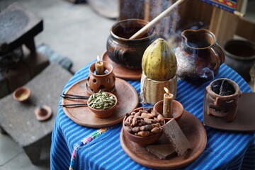 Various Guatemalan Mayan ingredientes on a table decorated with Mayan textile like cacao beans, vanilla beans, cacao pods, beeswax candles, cardamom.